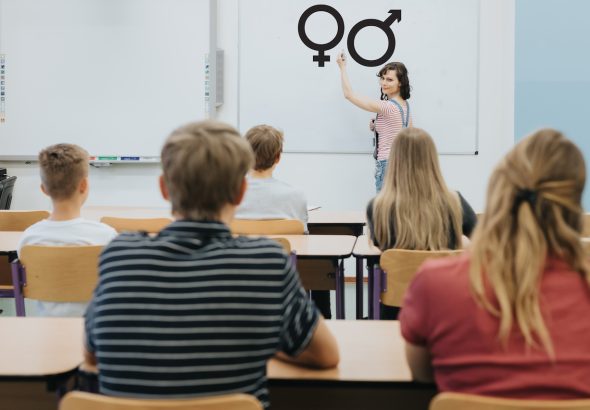 Joven profesora está de pie delante de la pizarra durante la lección de educación sexual